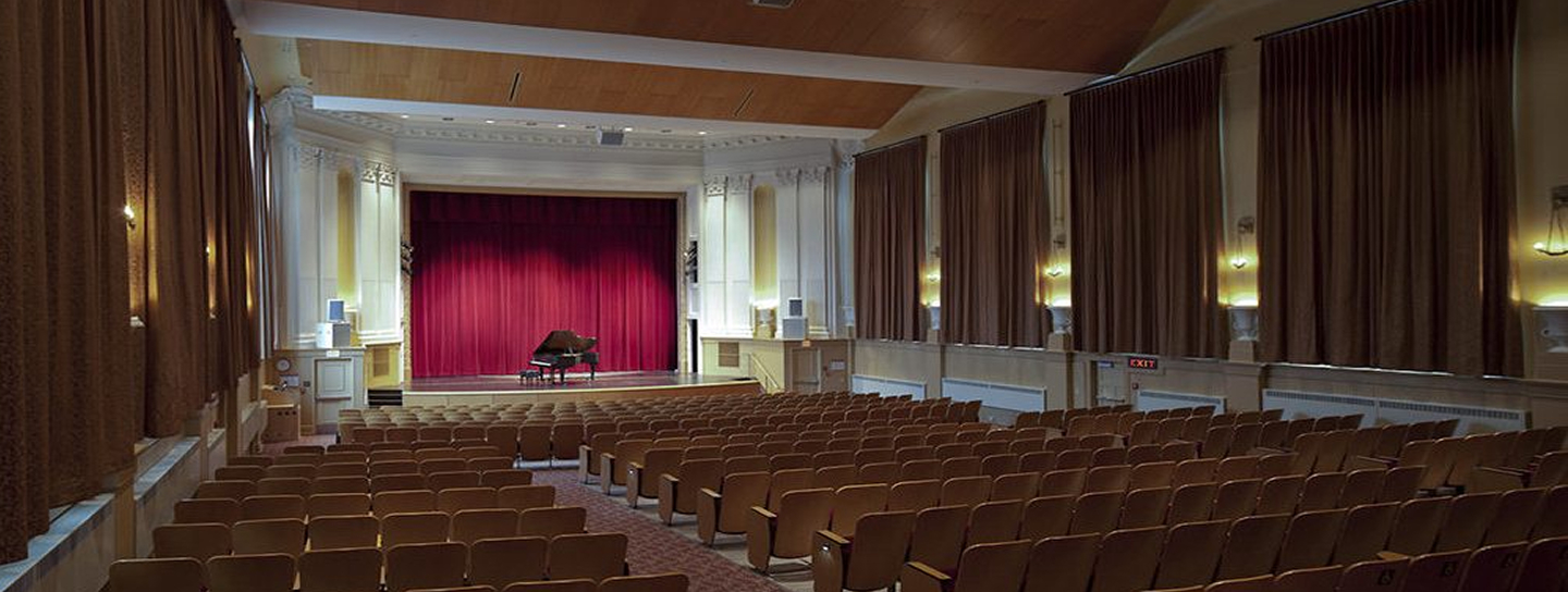 A spacious auditorium featuring a grand piano positioned centrally on the stage.
