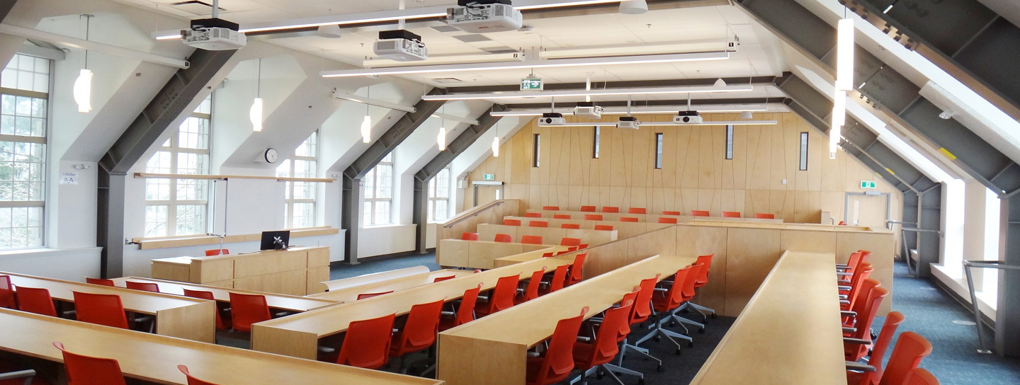 A lecture hall featuring multiple rows of red chairs arranged for an audience.